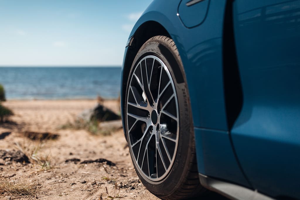 Nahaufnahme eines Sportreifens an einem blauen Auto am Strand als Symbolbild für den sportauto Sommerreifentest 2026 205/45 R17